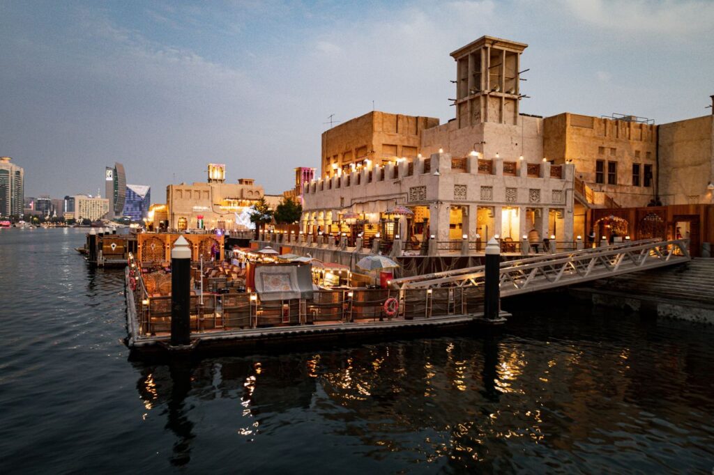 Crafting Captivating Headlines: Your awesome post title goes here Charming view of Dubai Creek's waterfront with illuminated buildings and a bustling restaurant scene.