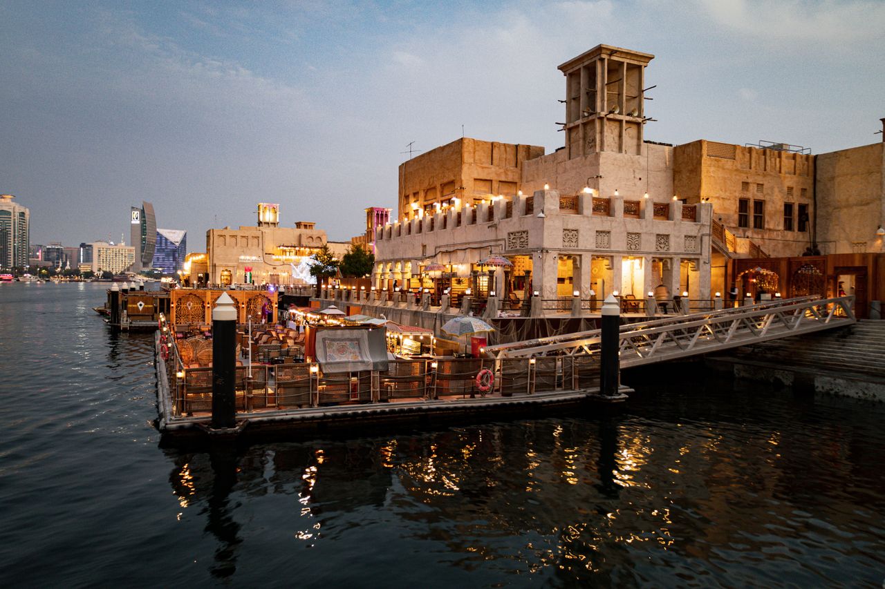 Crafting Captivating Headlines: Your awesome post title goes here Charming view of Dubai Creek's waterfront with illuminated buildings and a bustling restaurant scene.